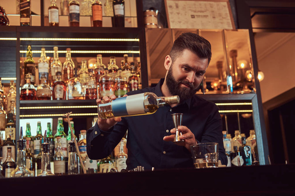 Elegante barman brutal en una camisa negra hace un cóctel en el fondo del mostrador del bar
. - Foto, Imagen