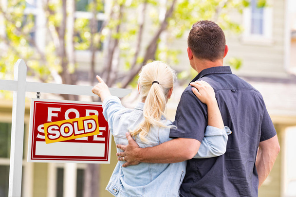 Kaukasisches Paar zeigt auf Schild und Haus einer verkauften Immobilie. - Foto, Bild