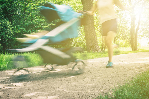 Femme de course avec poussette bébé profitant de l'été dans le parc. Jogging ou supermaman de marche de puissance, famille active avec bébé jogger, flou de mouvement
. - Photo, image
