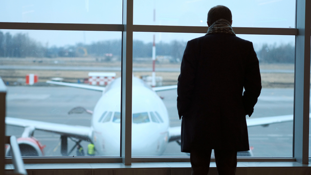 vecchio in piedi a tutta altezza, sguardo fuori dalla finestra terminale dell'aeroporto, vista silhouette. Guarda l'aereo all'aeroporto.
. - Filmati, video