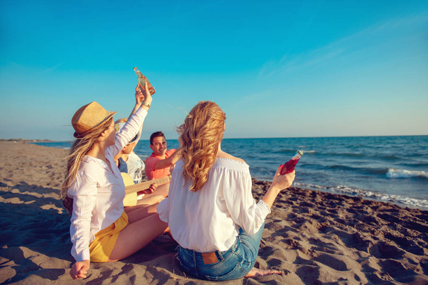Група щасливих молодих людей танцює на пляжі на красивому літньому заході сонця
 - Фото, зображення
