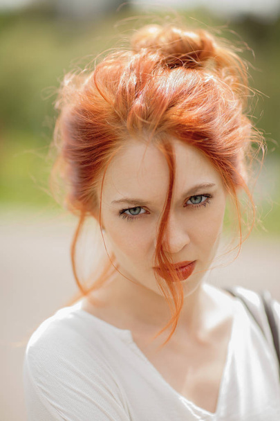 beautiful young woman with red hair, outside in a park in the sunlight, looking into the camera, lifestyle concept shoot - Foto, Imagen
