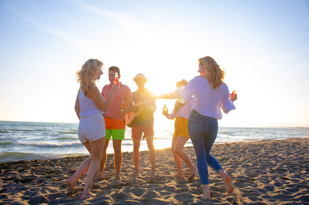 group of happy young people dancing at the beach on beautiful summer sunset - Фото, изображение