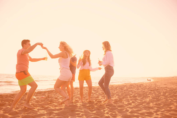 groep van gelukkige jonge mensen dansen op het strand op mooie zomerse zonsondergang - Foto, afbeelding