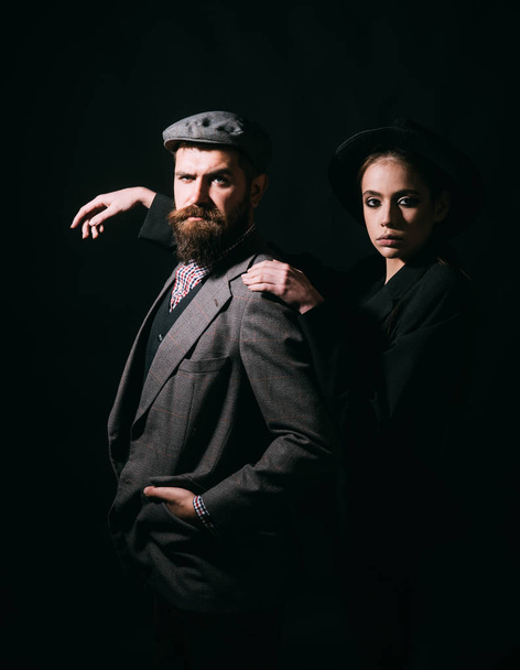 Couple in stylish classical outfits on black background, fashion concept. Bearded man in elegant suit wearing a cap. Family of aristocrats posing for portrait. - Valokuva, kuva