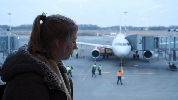 Menina ou adolescente vestindo óculos, em um lenço olhando para um avião no aeroporto, segurando seu passaporte e bilhete. Ela está atrasada e um pouco perdida. Rastreamento portátil
. - Filmagem, Vídeo