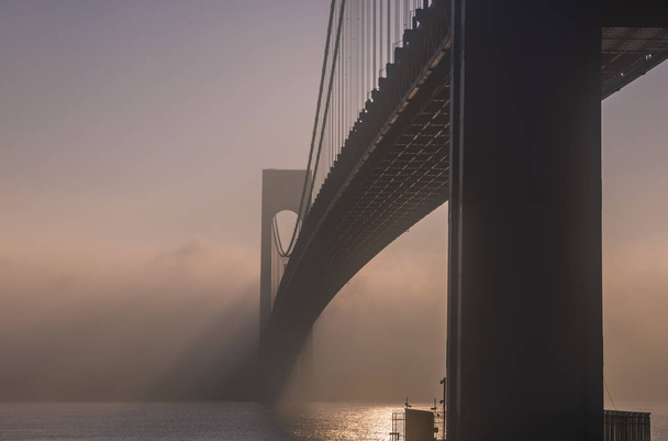 Increíble vista del puente en la niebla. El puente Verrazano-Narrows es un puente colgante de dos pisos que conecta los distritos de la ciudad de Nueva York de Staten Island y Brooklyn.
 - Foto, Imagen