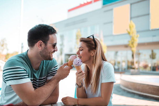 Счастливая молодая пара сидит перед торговым центром и ест мороженое
 - Фото, изображение