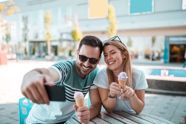 アイスクリームを食べながら彼のガール フレンドと selfie を取ってサングラスを探している好青年 - 写真・画像