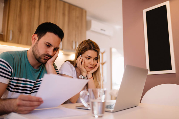 Worried young couple analyzing bills while sitting in kitchen - Foto, imagen