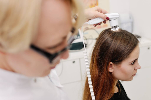 Dermatologe untersucht Haare einer Patientin mit einem speziellen Gerät - Foto, Bild