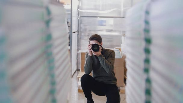 Joven fotógrafo profesional disparando delante de pilas de papel en la tipografía
 - Foto, Imagen