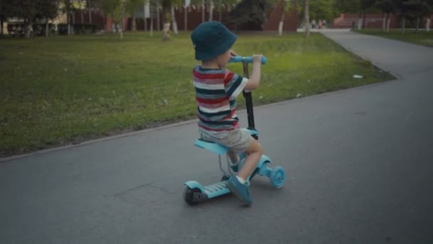 Szczęśliwy mały chłopiec dwa lata stary, jazda skuterem w parku lato - Materiał filmowy, wideo