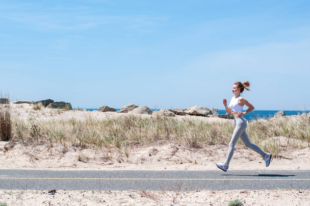 Fitness woman running on beach. Happy sporty woman jogging outdoors - Valokuva, kuva