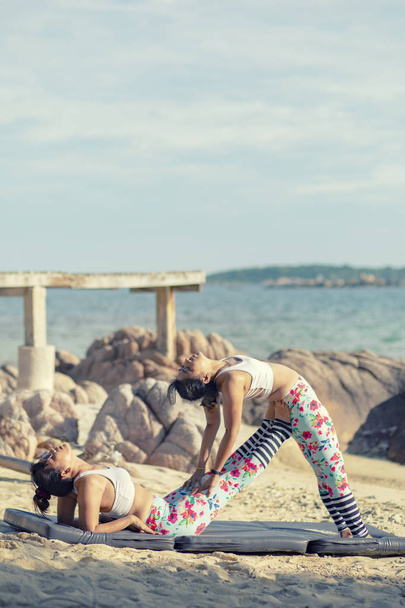 две азиатки, играющие в позу йоги на морском пляже
  - Фото, изображение