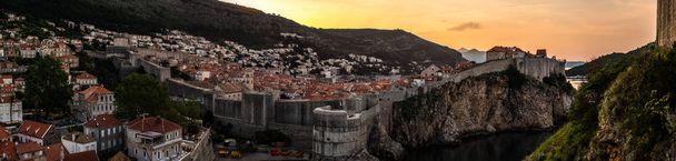 wunderschönes Panorama des gelben und orangen Himmels Sonnenaufgang Blick auf die historische Altstadt in Dubrovnik Kroatien umgeben von Steinmauern mit Hügeln in der Ferne von einem hohen Aussichtspunkt. - Foto, Bild