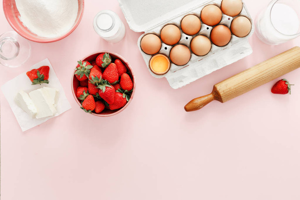Raw ingredients for making strawberry pie or cake on pink background (eggs, flour, milk, sugar, strawberry) with copy space, top view, flat lay. Bakery background. Recipe for strawberry pie - Fotografie, Obrázek