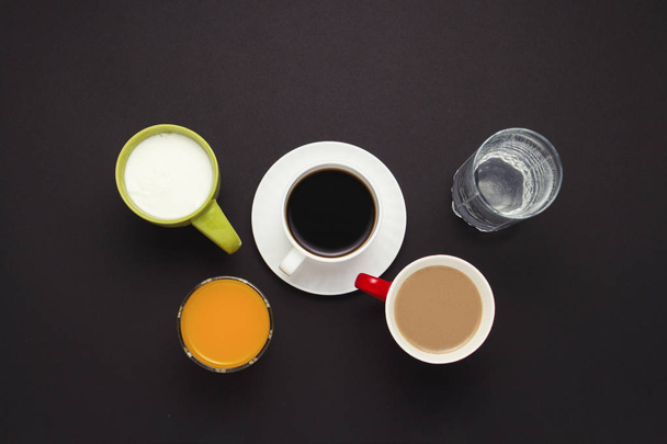 Taza blanca con café, Just Water, Zumo de naranja en un vaso, Yogur, Café con leche sobre fondo oscuro. Estilo minimalista. Piso tendido, vista superior
. - Foto, Imagen