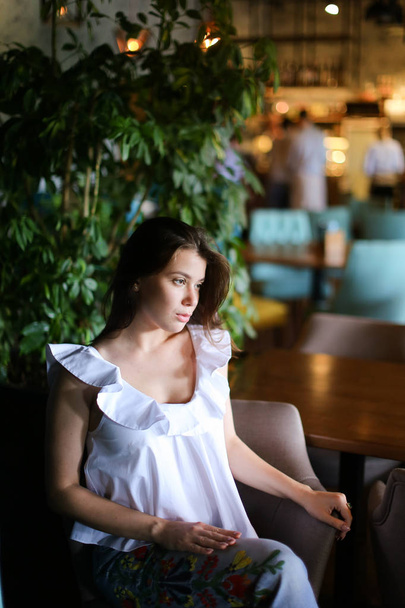 Pretty businesswoman sitting at cafe and wearing white blouse with ethnic jeans. - Foto, imagen