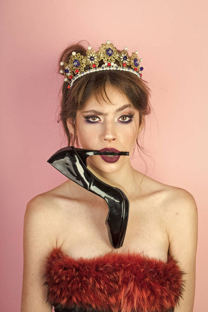 Beautiful brunette girl with a golden crown and professional evening make-up. Beauty face with shoe in mouth. - Fotó, kép