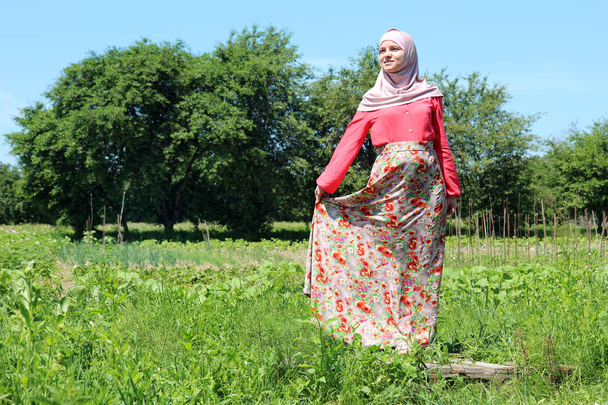 беременная молодая женщина в разноцветной мусульманской одежде позирует перед камерой на природе
 - Фото, изображение