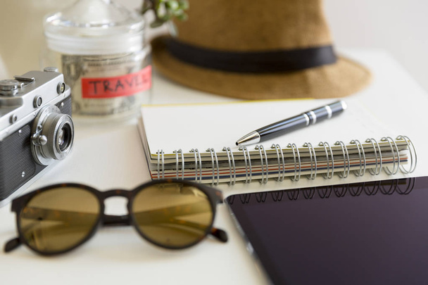 Concepto de planificación de viajes sobre la mesa. Accesorios y artículos del viajero con cuaderno y frasco de ahorro de dinero, gafas de sol y sombrero
 - Foto, Imagen