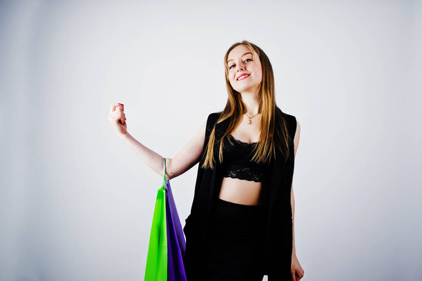 Girl model in black wear with colored shopping bags posed at studio on white background.  - Foto, imagen