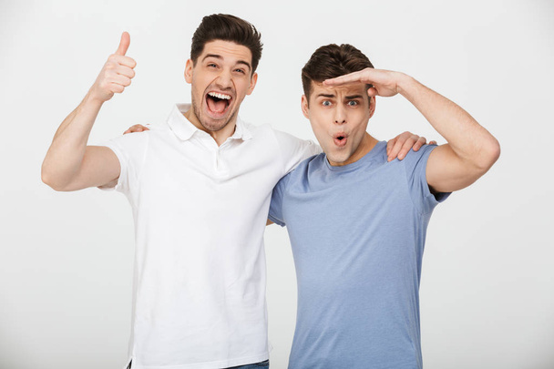 Photo of two male friends 30s wearing casual t-shirt and jeans hugging and posing on camera with smile isolated over white background - Fotoğraf, Görsel