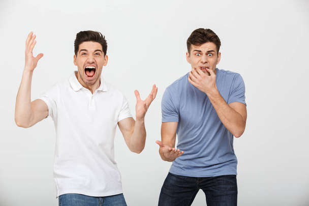 Photo of two emotional men 30s wearing casual t-shirt and jeans shouting and rooting for team isolated over white background - Fotoğraf, Görsel