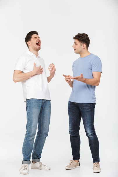 Full length portrait of two handsome young men talking and laughing isolated over white background - Fotografie, Obrázek