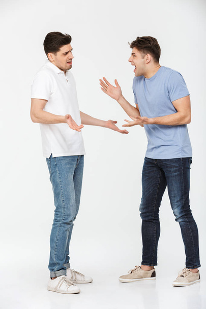 Full length portrait of two frustrated young men arguing isolated over white background - Fotoğraf, Görsel