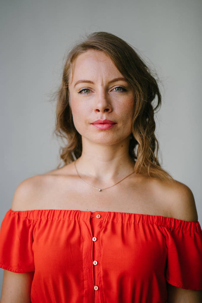 Portrait of a young, attractive European woman in an orange summer dress posing . She is blond with green eyes and is smiling confidently. - Фото, зображення