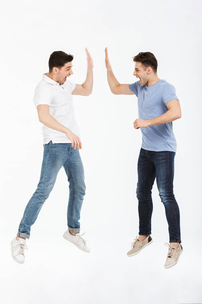 Full length portrait of two happy young men giving high five isolated over white background - Φωτογραφία, εικόνα