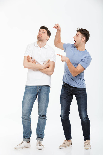 Full length portrait of two confused young men pointing fingers isolated over white background - Фото, зображення