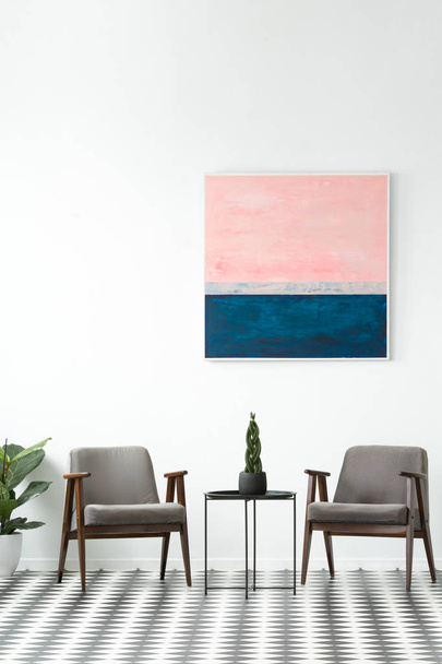 Plant on a table between grey armchairs in modern interior with pink and blue painting on white wall - Φωτογραφία, εικόνα