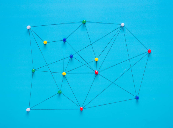 Small network of pins (Thumbtack)and string, An arrangement of colourful pins linked together with string on a pale background suggesting a network of connections. - Foto, Bild