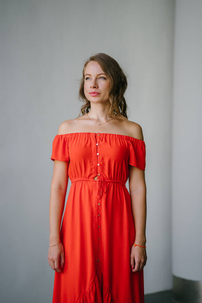 Portrait of a young, attractive European woman in an orange summer dress posing . She is blond with green eyes and is smiling confidently. - Foto, Imagem
