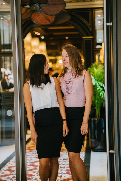 Portrait of a diverse team of two coworkers (a Chinese Asian woman and a Caucasian woman) standing next to one another against a green wall of plants. They are smiling and laughing in a relaxed way. - Foto, immagini