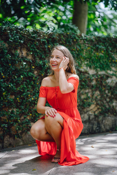 Retrato de una joven y atractiva mujer europea en un vestido de verano naranja posando. Ella es rubia con ojos verdes y sonríe con confianza
. - Foto, imagen