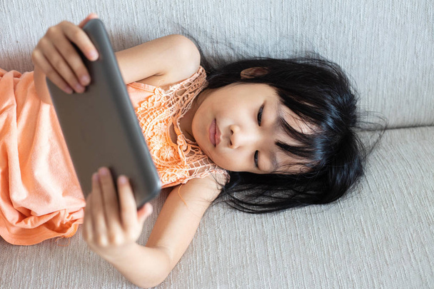 Asian Chinese little girl using tablet lying on the sofa in the living room - Foto, immagini