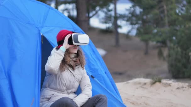 Kırmızı bir şapka çekici genç kadın turist turist çadırda oturur ve bir sanal gerçeklik kask sahiptir - Video, Çekim