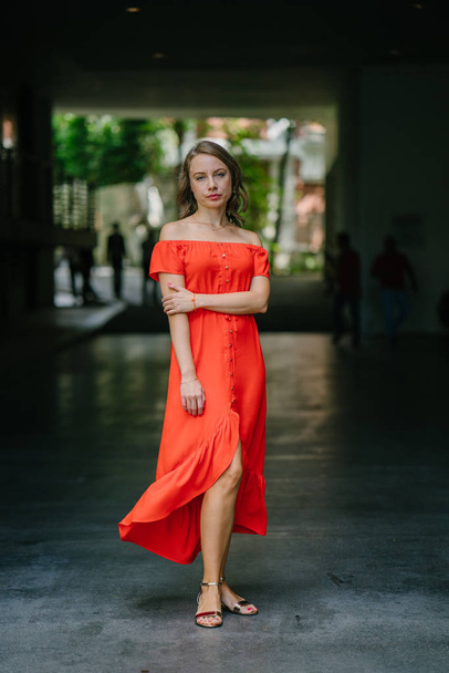 Portrait of a young, attractive Caucasian woman walking outdoor in park in the day. She was wearing a beautiful, light and comfortable orange dress and is smiling playfully. - Valokuva, kuva