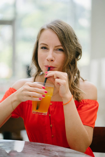 Portrait of a young, attractive European woman in an orange summer dress with drink . She is blond with green eyes and is smiling confidently. - Foto, immagini