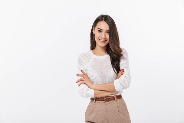 Portrait of a smiling asian businesswoman standing with arms folded and looking at camera isolated over white background - Foto, Imagem