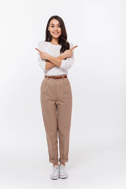 Full length portrait of a smiling asian businesswoman standing and pointing fingers both ways isolated over white background - Fotó, kép