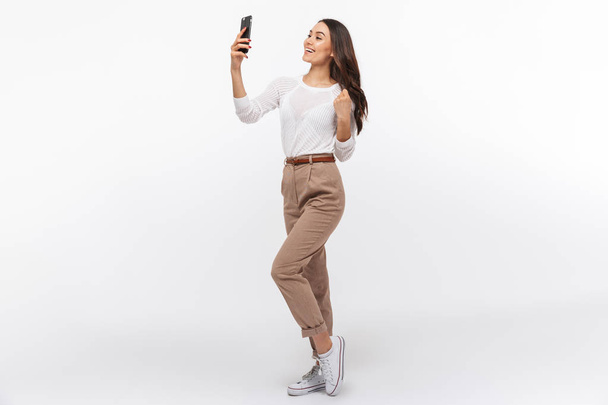 Full length portrait of a smiling asian businesswoman taking selfie with mobile phone isolated over white background - Фото, изображение