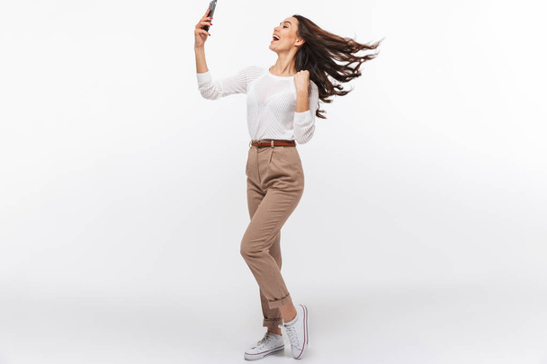 Full length portrait of a laughing asian businesswoman taking selfie with mobile phone isolated over white background - Zdjęcie, obraz