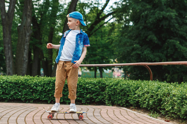A small city boy and a skateboard. A young guy is riding in a park on a skateboard. City Style. City children. A child learns to ride a skateboard - Zdjęcie, obraz