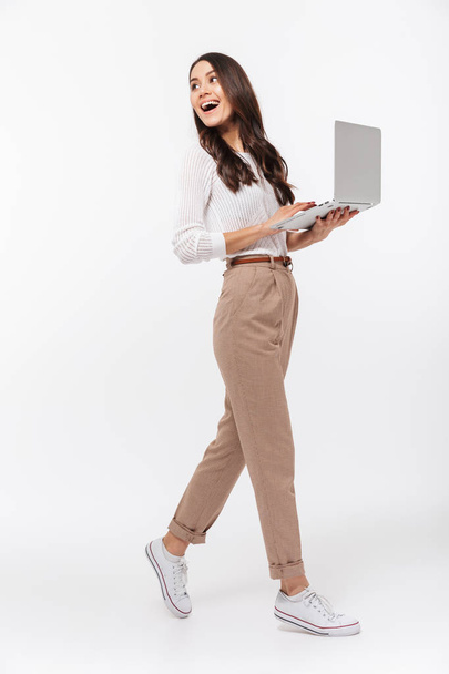 Full length portrait of a happy asian businesswoman holding laptop computer and looking away isolated over white background - Foto, immagini