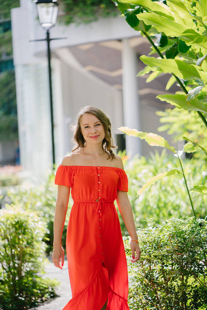 Portrait of a young, attractive Caucasian woman walking outdoor in park in the day. She was wearing a beautiful, light and comfortable orange dress and is smiling playfully. - Foto, immagini
